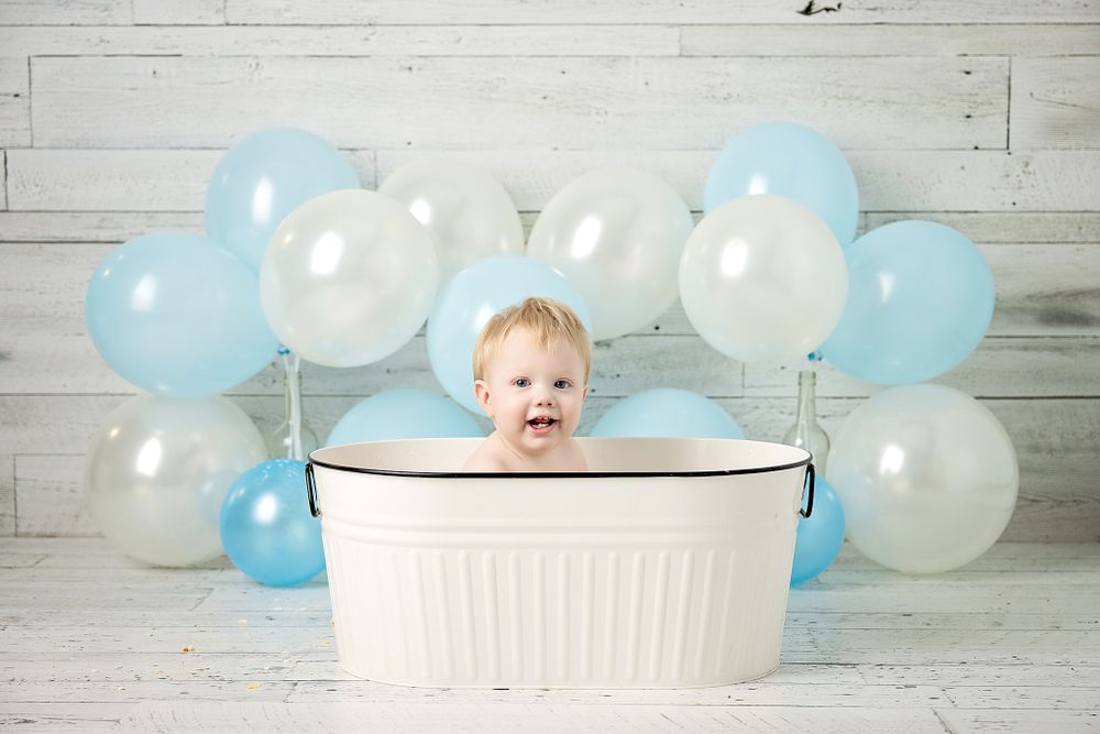 Joyful bath time photo with white tub and festive balloon backdrop.