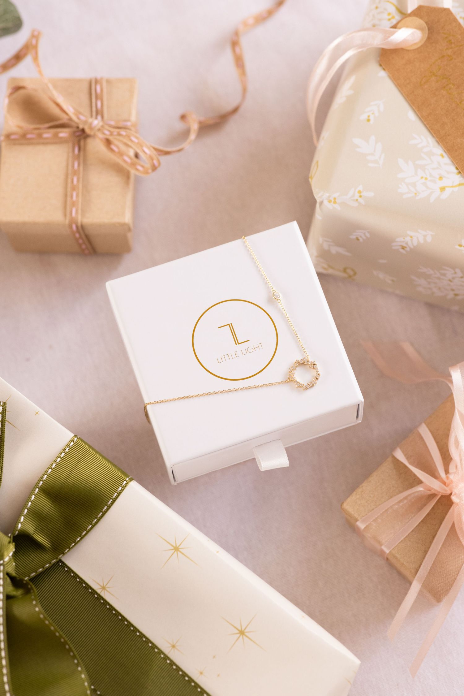 Elegantly wrapped gift boxes with gold accents and ribbons in white, green and natural tones. Diamond encrusted necklace sits on a giftbox.