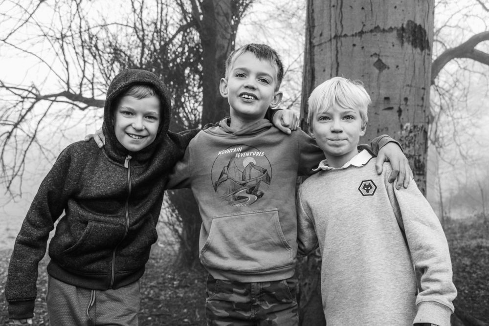 Three smiling children huddle together outdoors on a misty winter day.