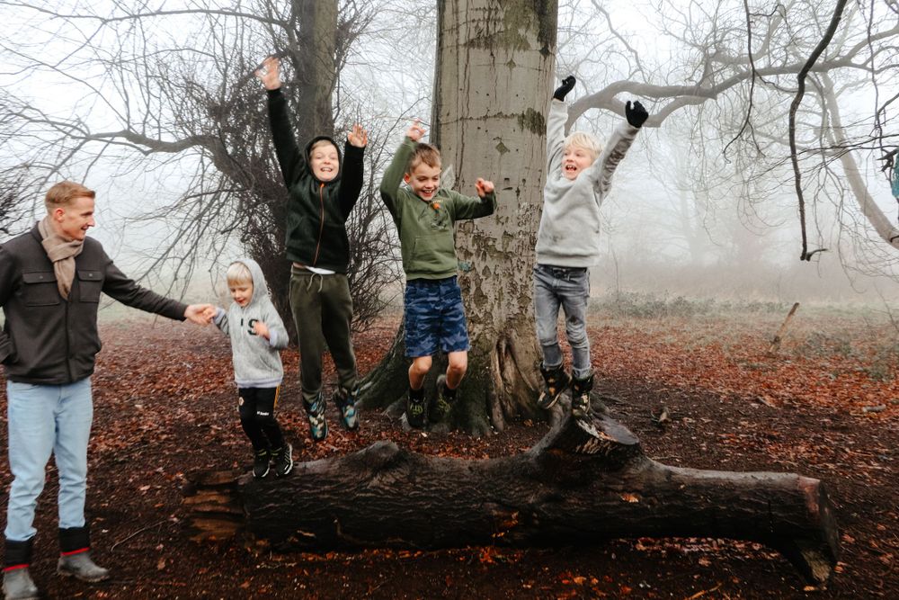 Children jumping and playing around a large tree trunk in a foggy autumn forest.