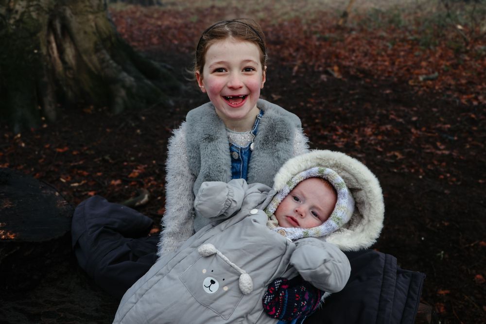 Two children laughing together while sitting on fallen leaves in winter.