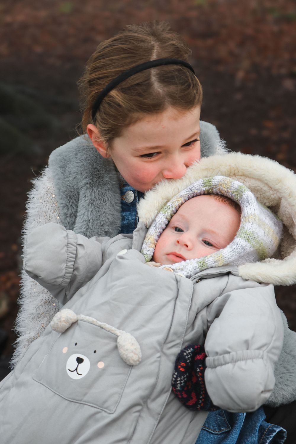 Winter outdoor portrait of siblings with younger one wearing a cute bear snowsuit.