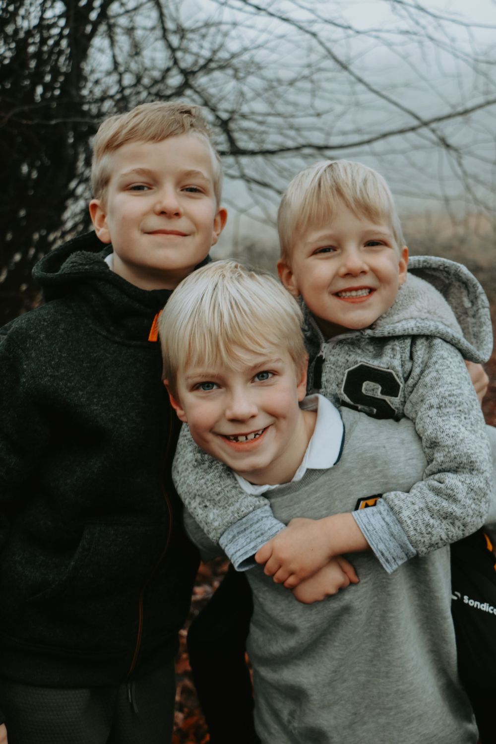 Three young children in casual wear smiling together outdoors.