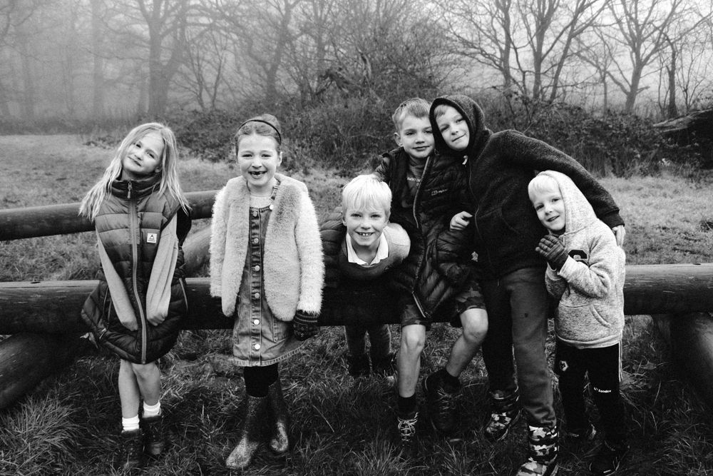 Black and white photo of a group sitting together on wooden logs in a natural setting.