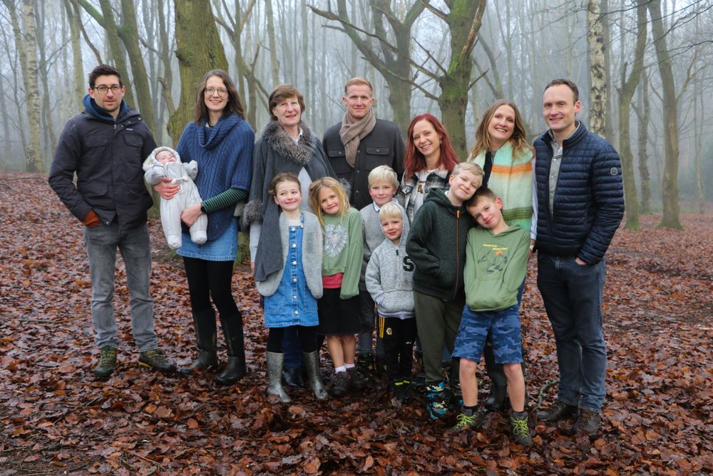 Extended family group poses together in a misty forest with fallen leaves on the ground.