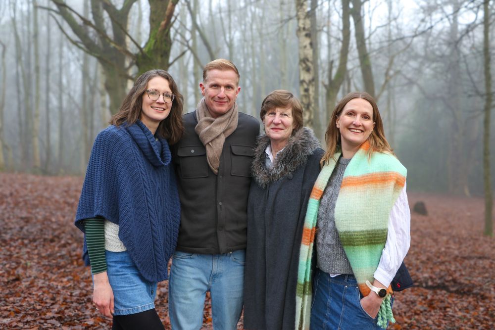 Four people stand together for a casual portrait in a foggy autumn forest.