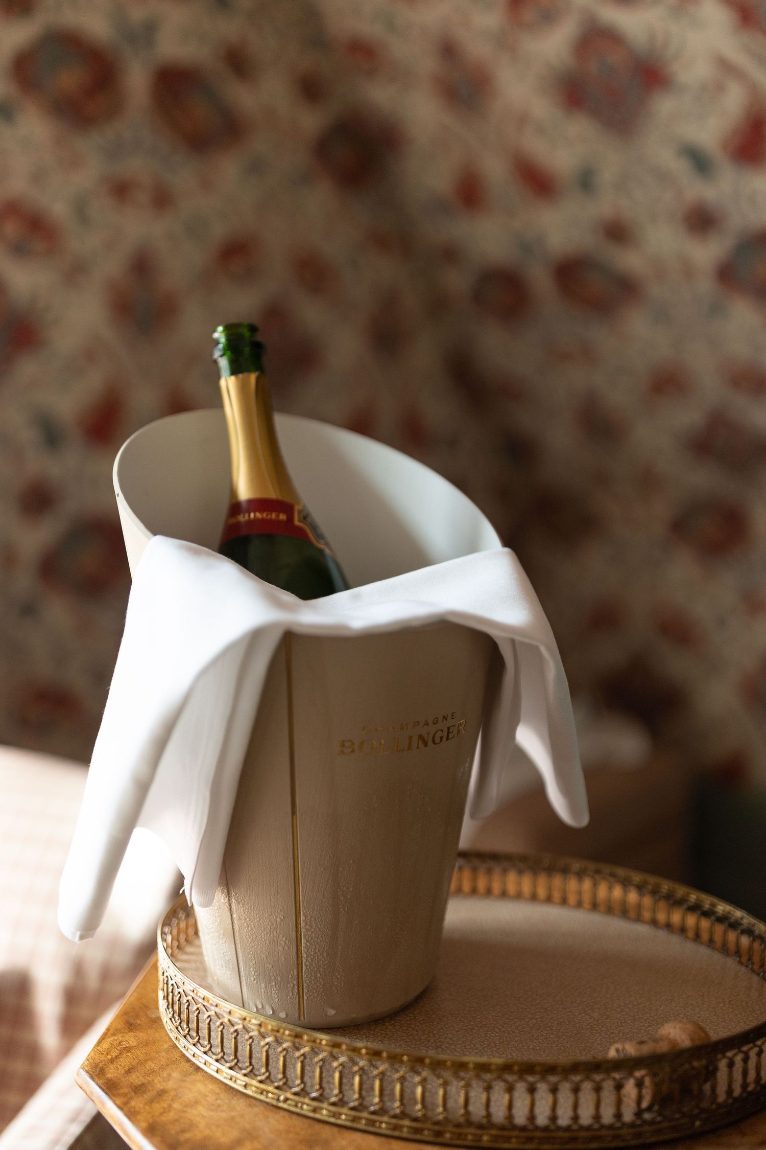 Champagne bottle wrapped in white napkin displayed in elegant gold-rimmed serving vessel.