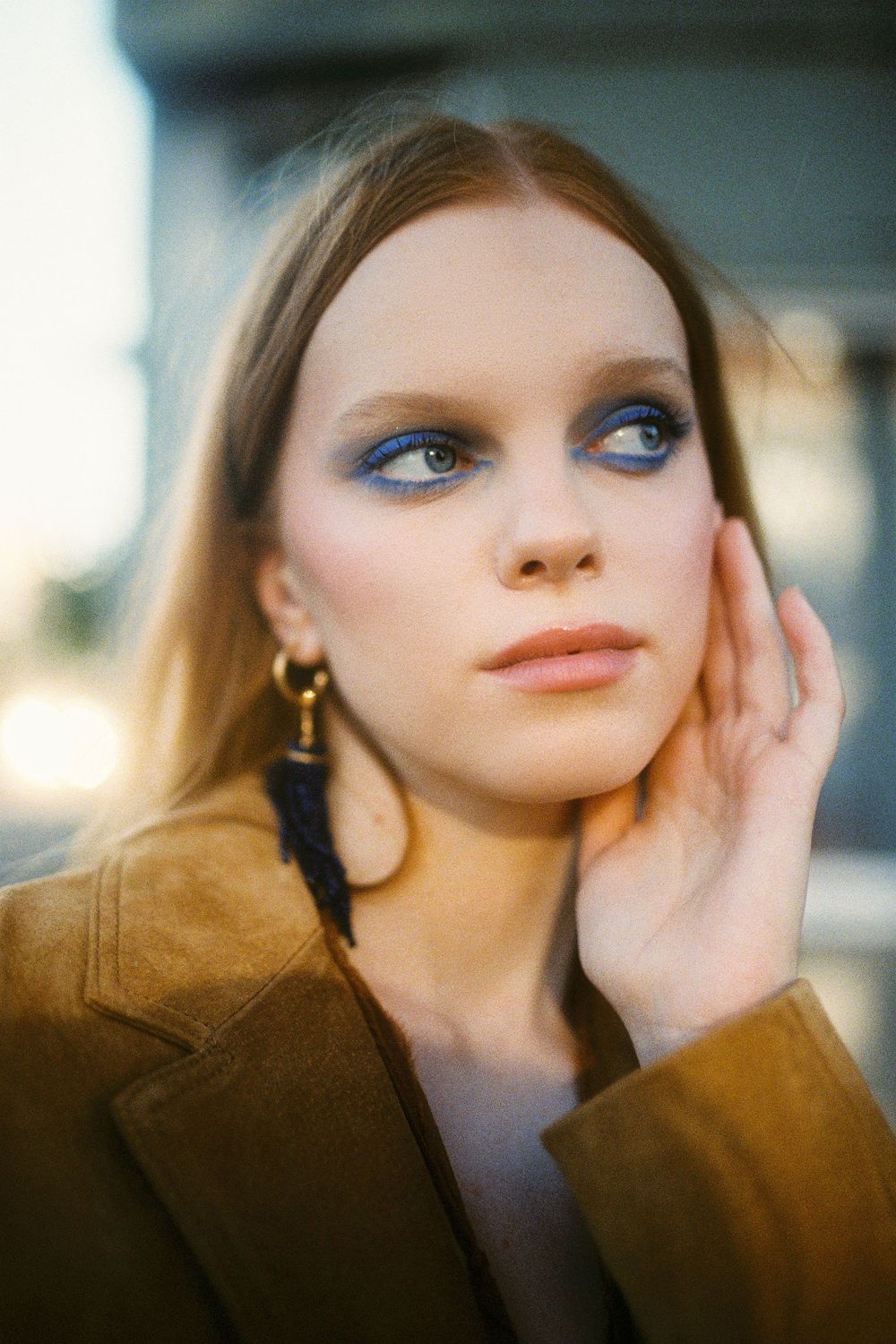 Close up fashion portrait with dramatic eye makeup, tassel earrings and suede jacket in warm natural lighting.