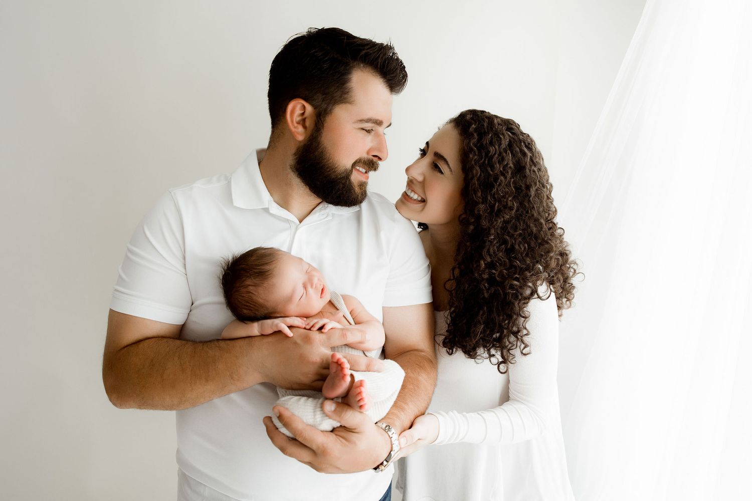 Newborn baby boy posed in dad's hands with dad and mom looking at each other