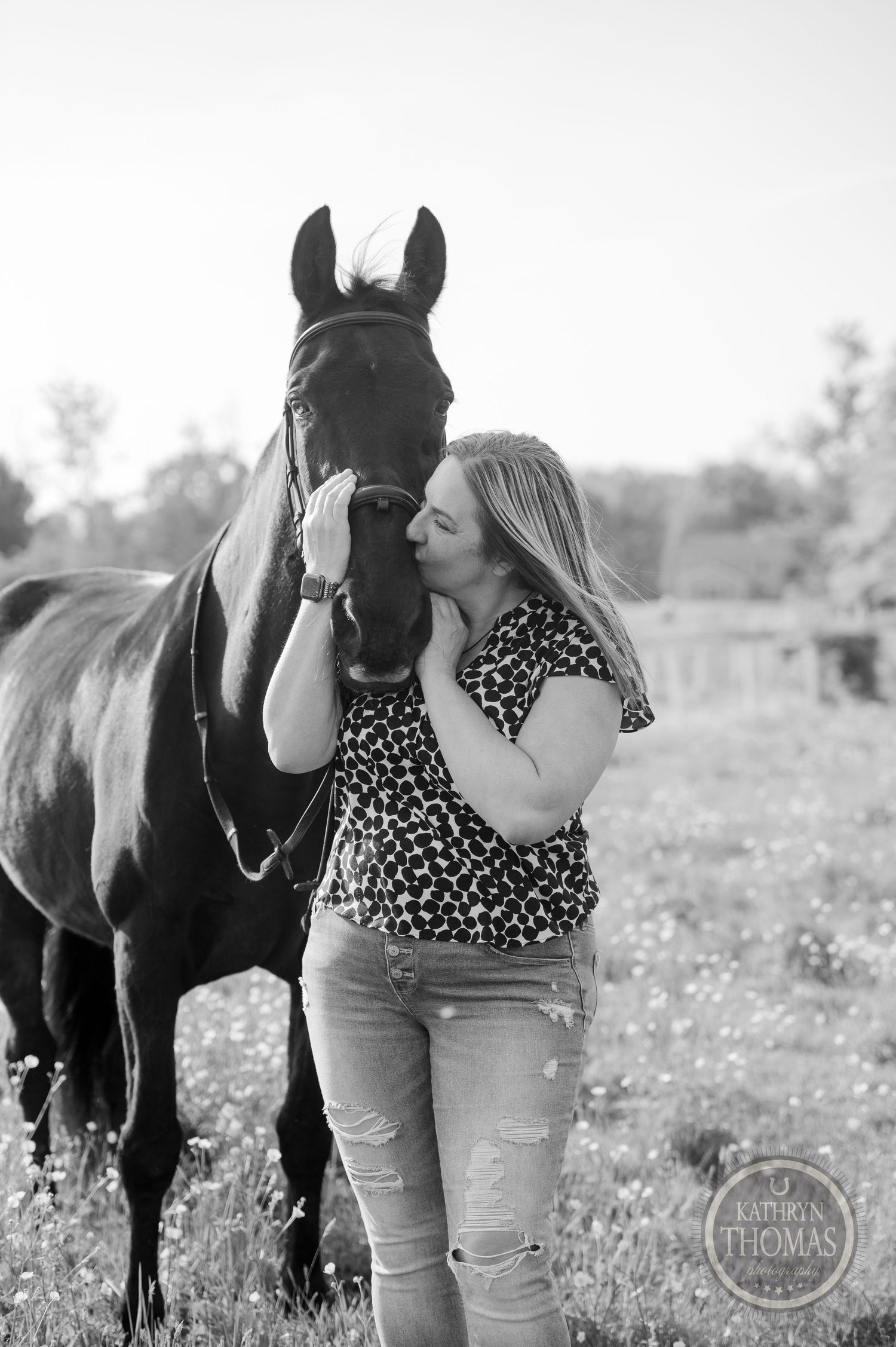 A tender moment between a dark horse and someone in a floral print top in a sunny meadow.