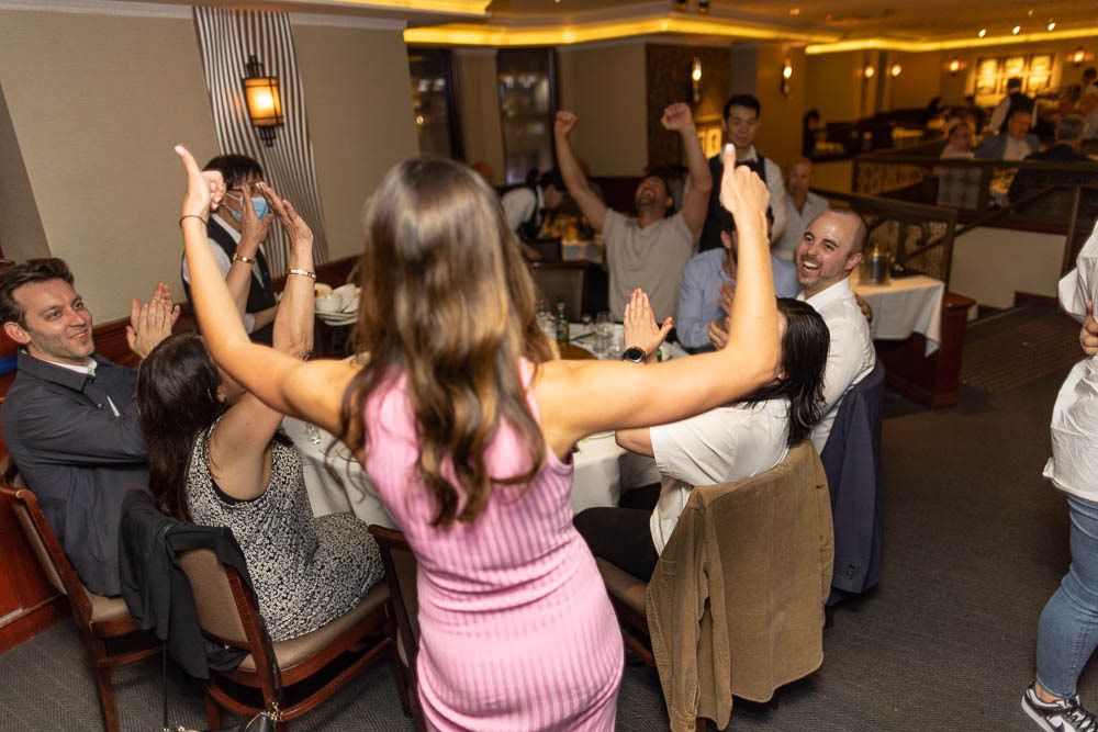 Wedding reception guests dancing and celebrating with raised arms in a dimly lit venue.