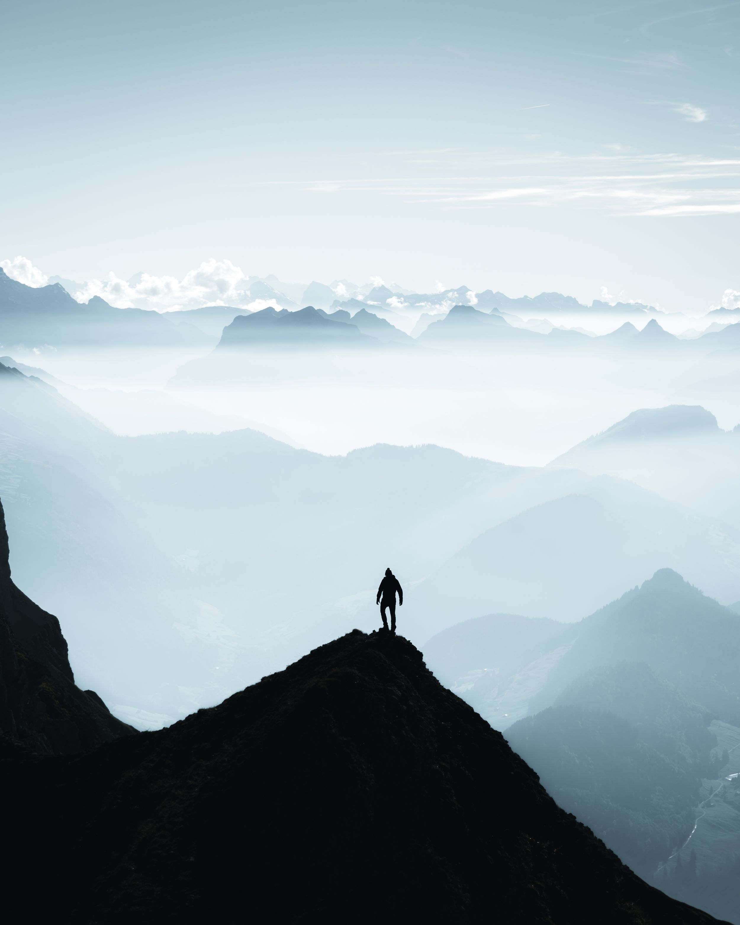 Silhouetted hiker on mountain peak against misty mountain range backdrop.