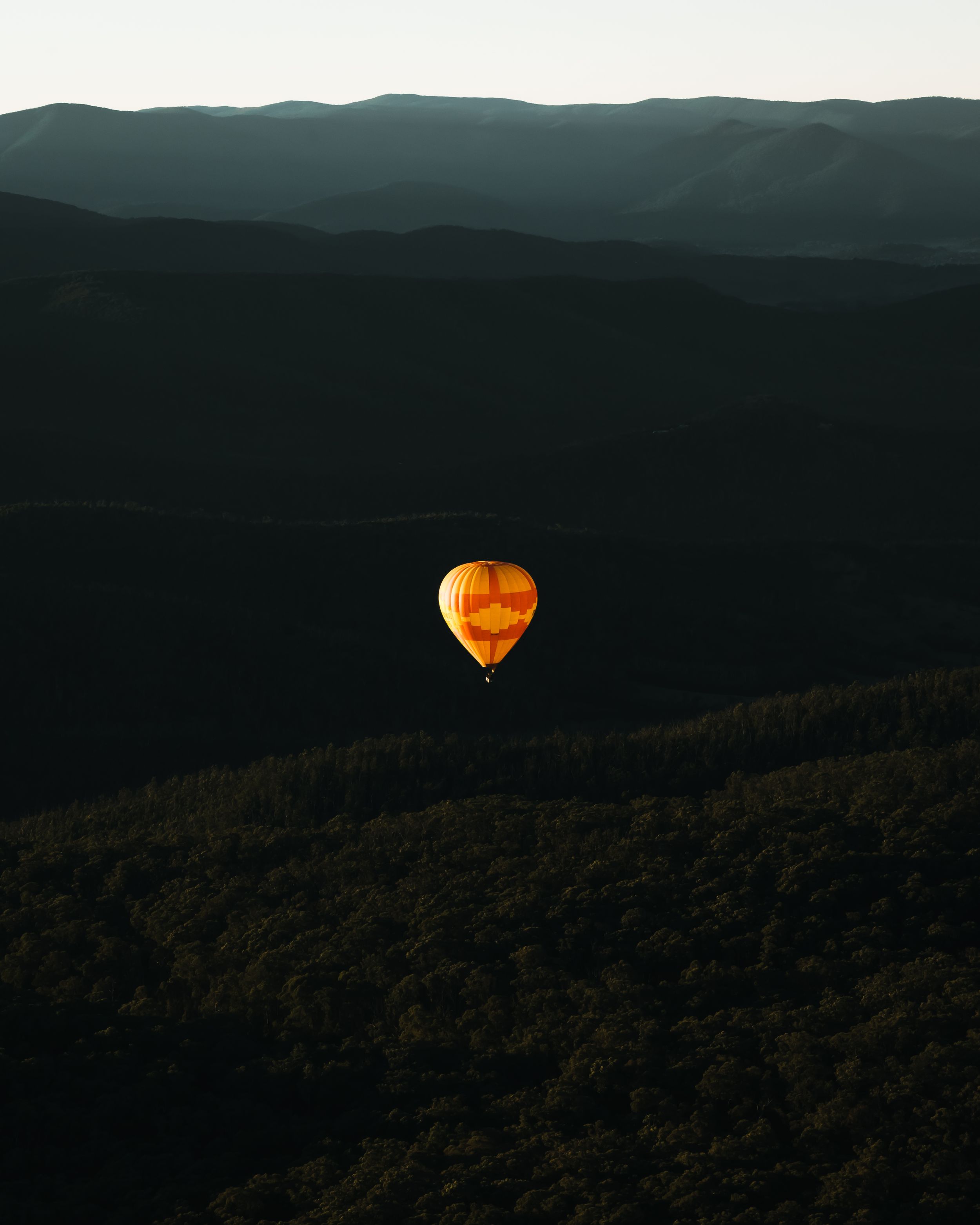 An illuminated hot air balloon glows orange against a dark mountain landscape at dusk.