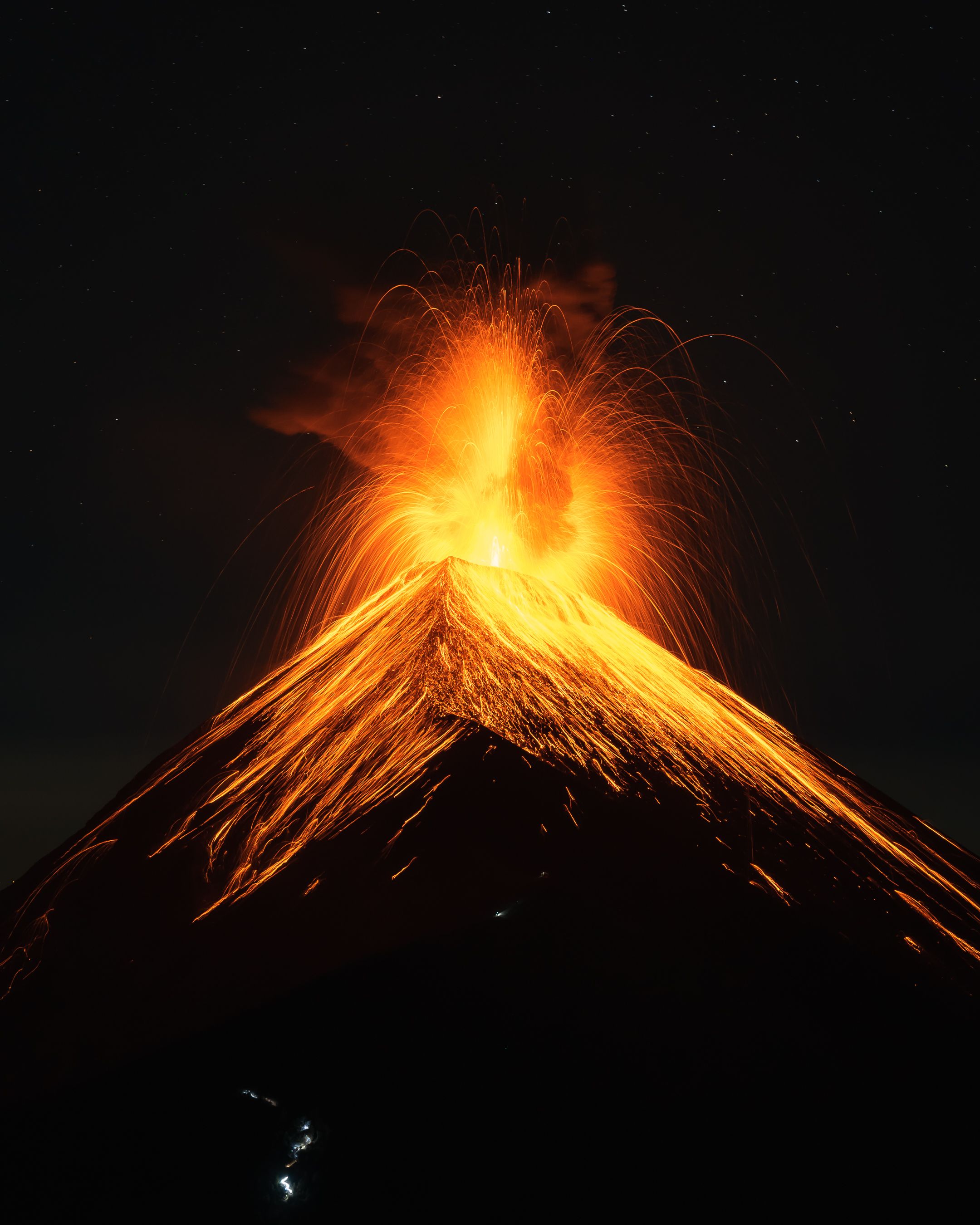 Dramatic nighttime volcanic eruption with glowing orange lava and ash plumes against dark sky.