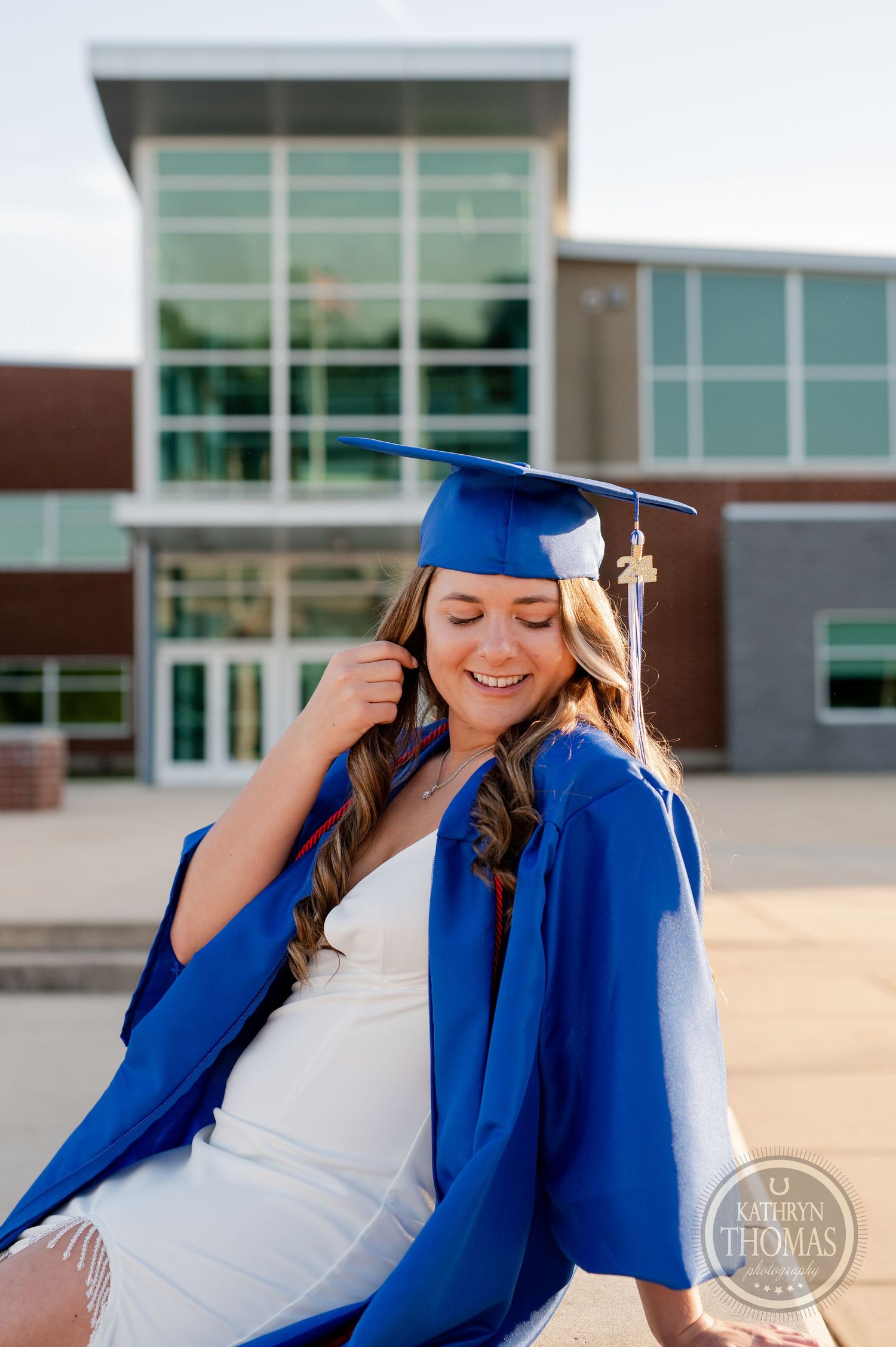 Graduate in royal blue gown and cap smiles joyfully during outdoor photo session.
