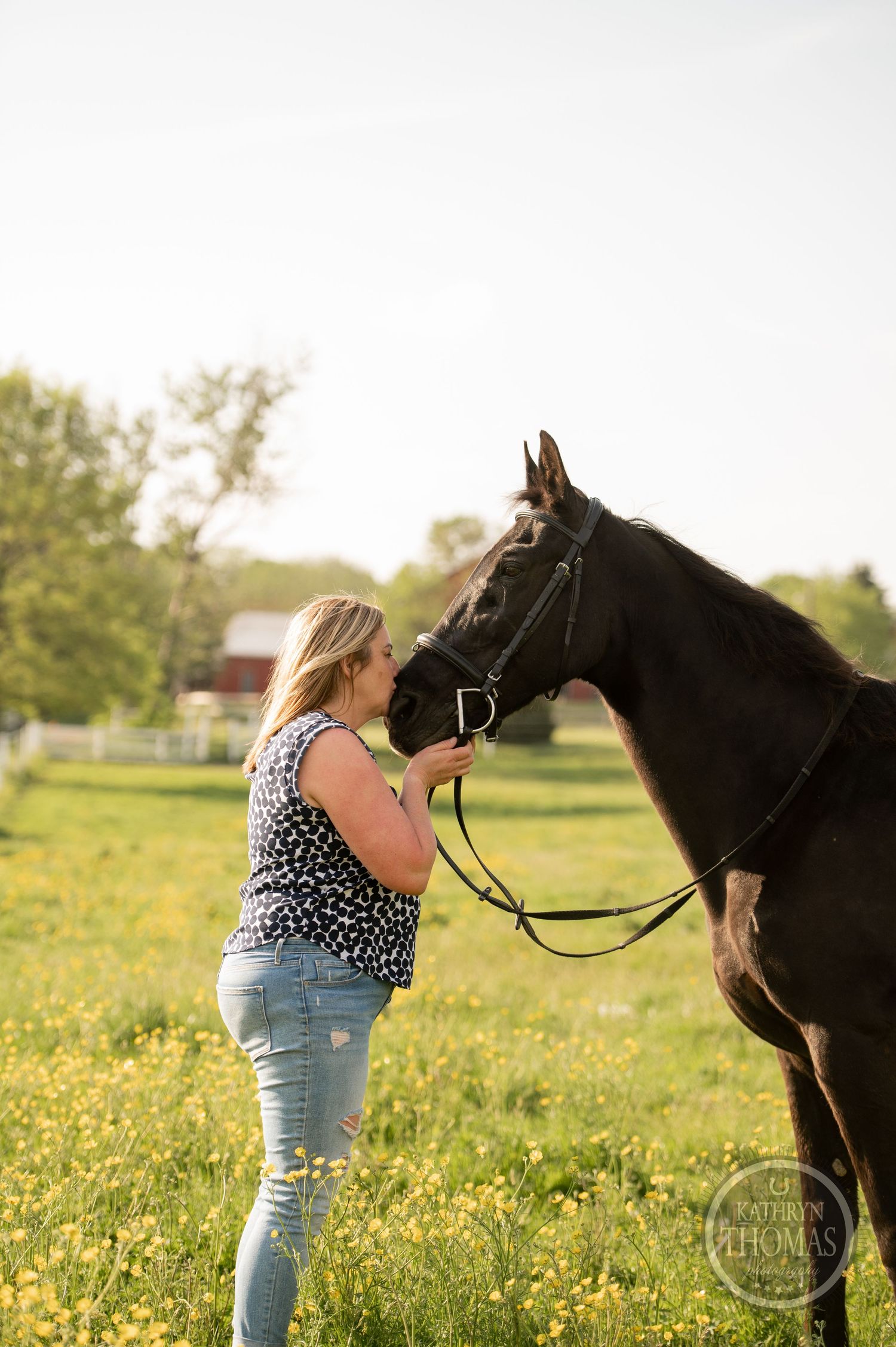 Tender interaction between a black horse and someone wearing a spotted top in a flowery field.