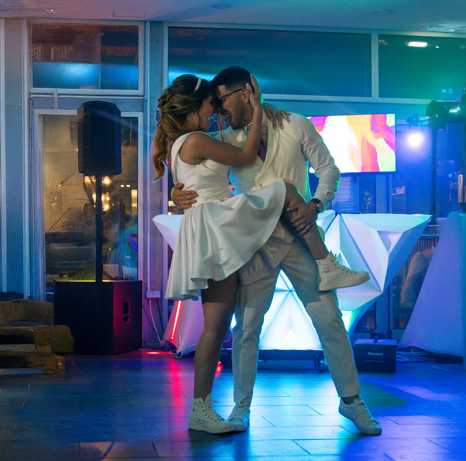 A couple performs a romantic dance dip in formal attire under blue lighting at their reception.