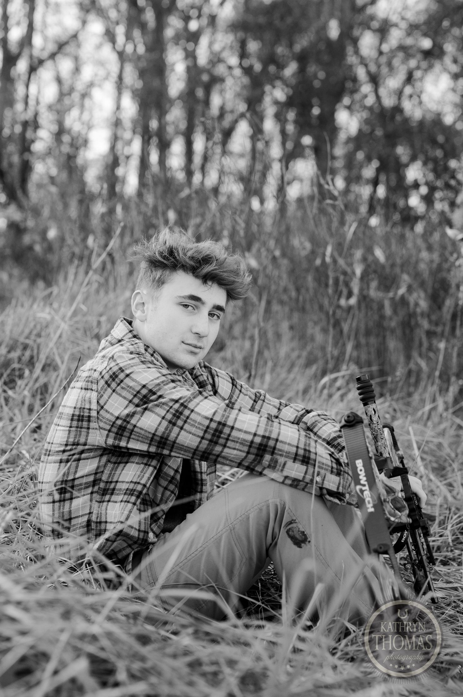 Black and white portrait of archer resting with bow in tall grass.