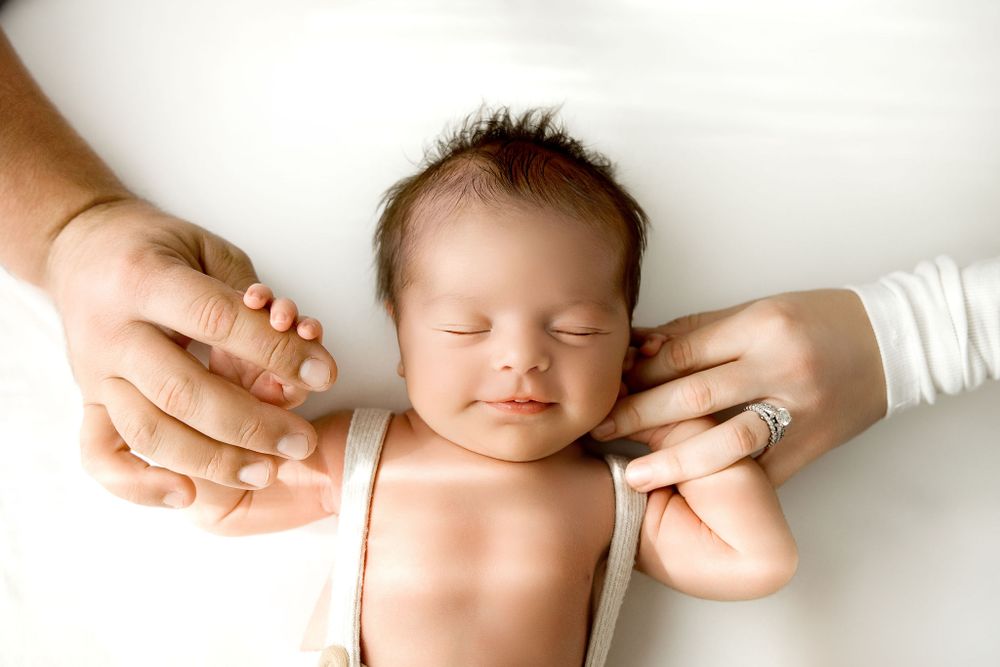 Newborn baby smiling, mother and father holding baby's hands