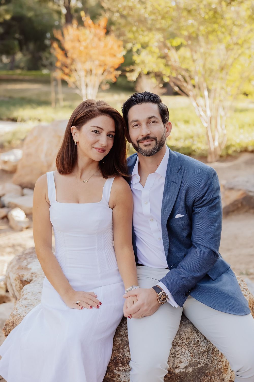 Couple in formal attire poses together on outdoor garden bench.