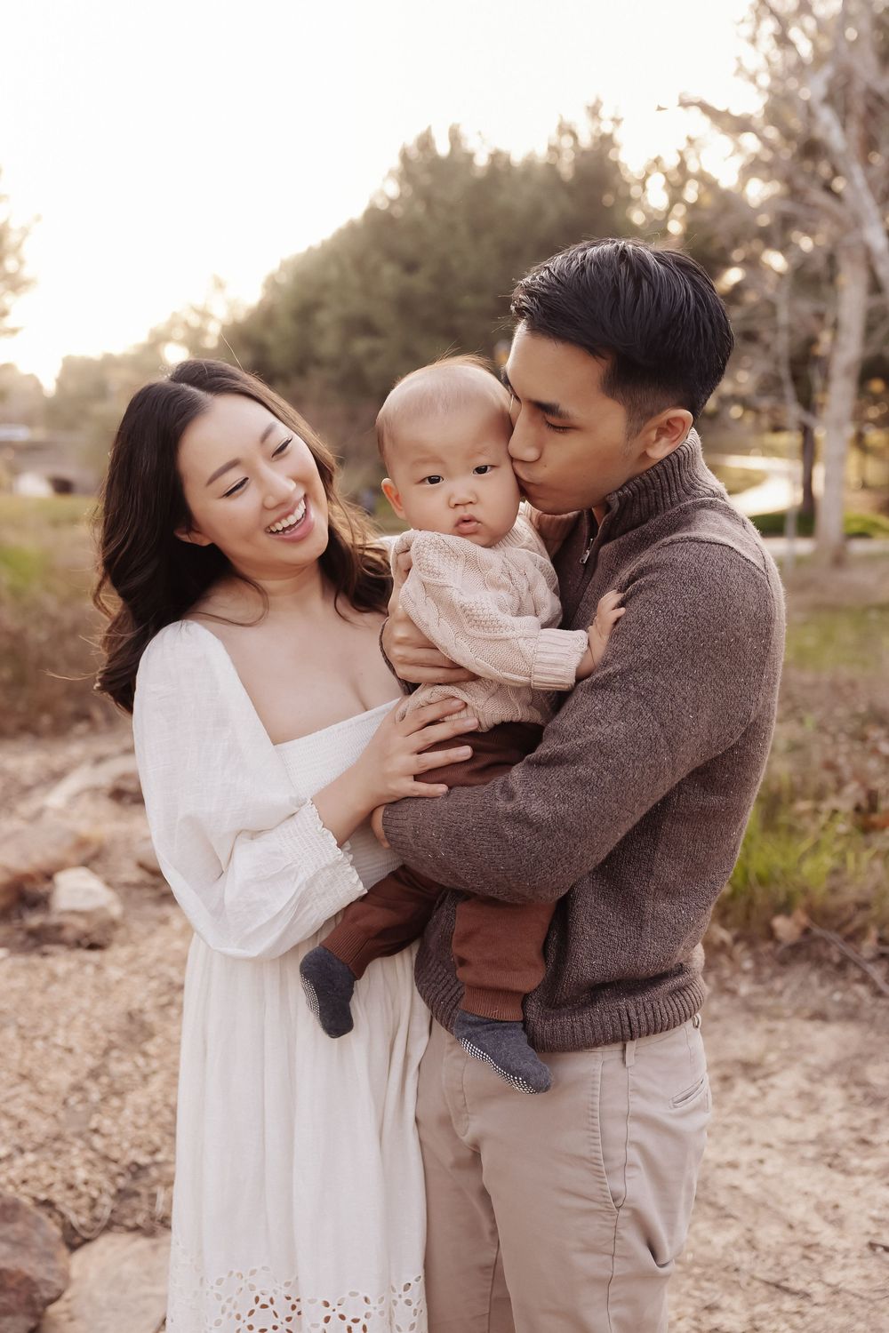 Young family sharing a tender moment outdoors in casual attire during golden hour lighting.