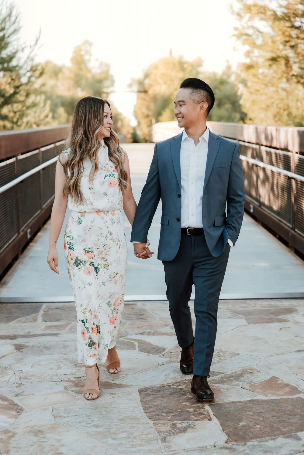 A couple laughs and holds hands while walking together along a rustic wooden bridge during a warm autumn sunset.