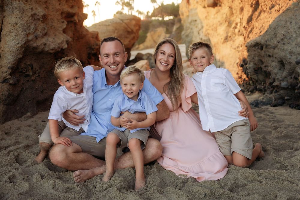 A family sitting together on a sandy beach with rocky cliffs in the background during golden hour.