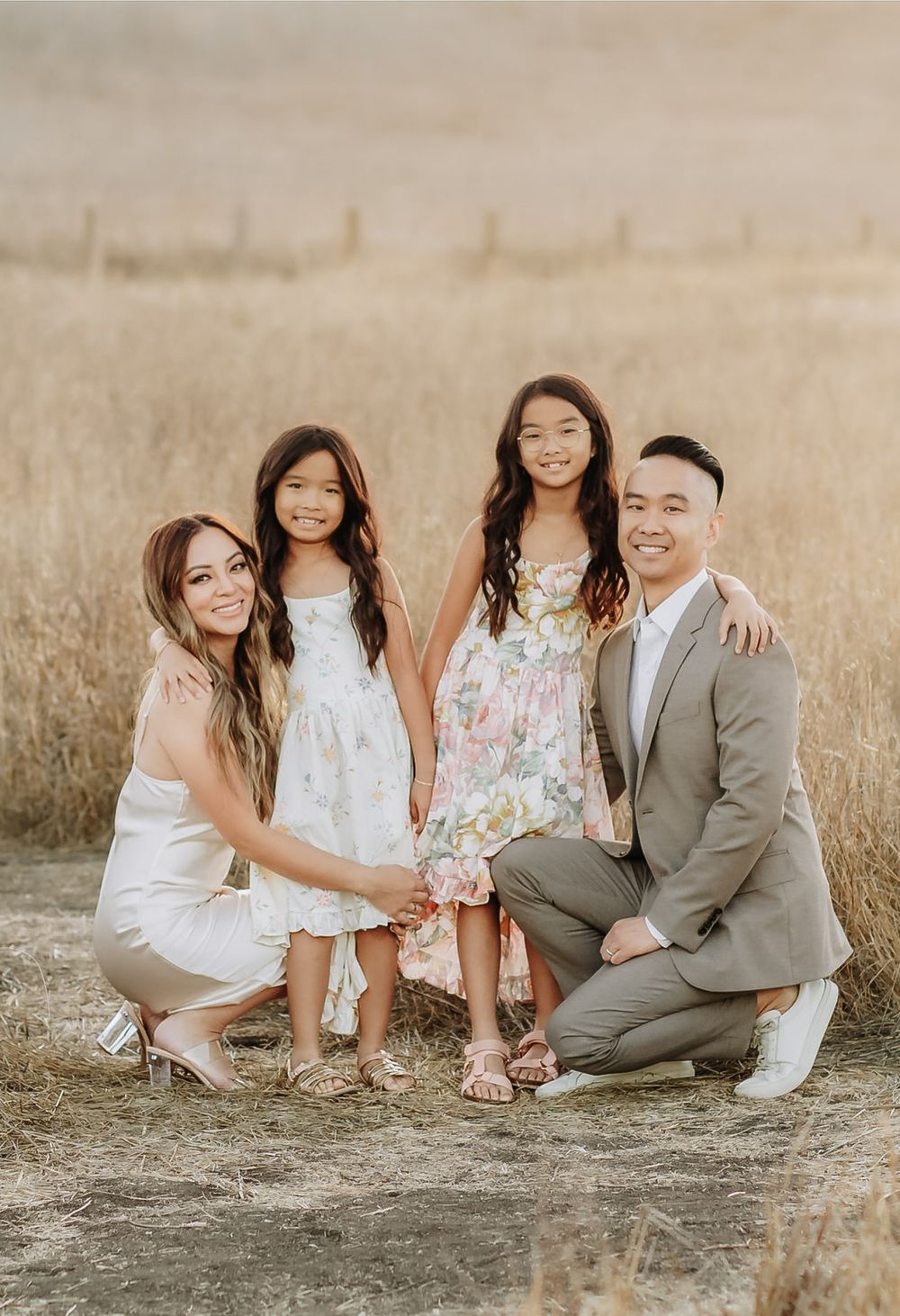 A family of four poses together in a sun-lit field of tall golden grass during a photo session.