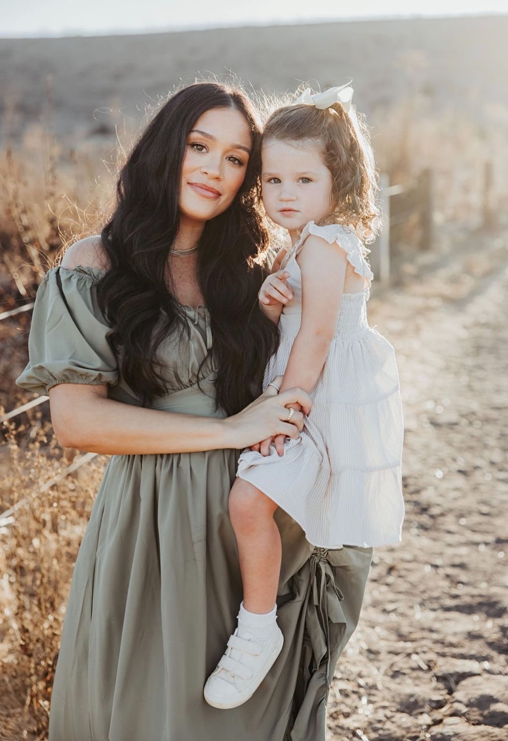An intimate outdoor portrait in a sunlit field with golden dried grass and soft evening light.