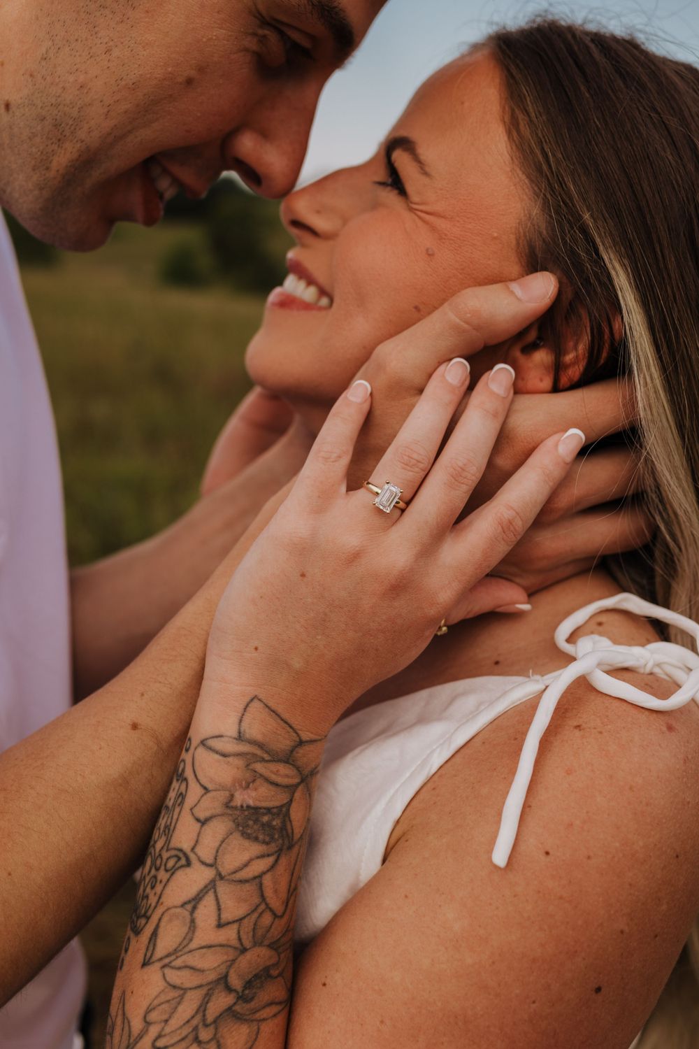 A close-up intimate moment between a couple showing an engagement ring and floral tattoo detail.