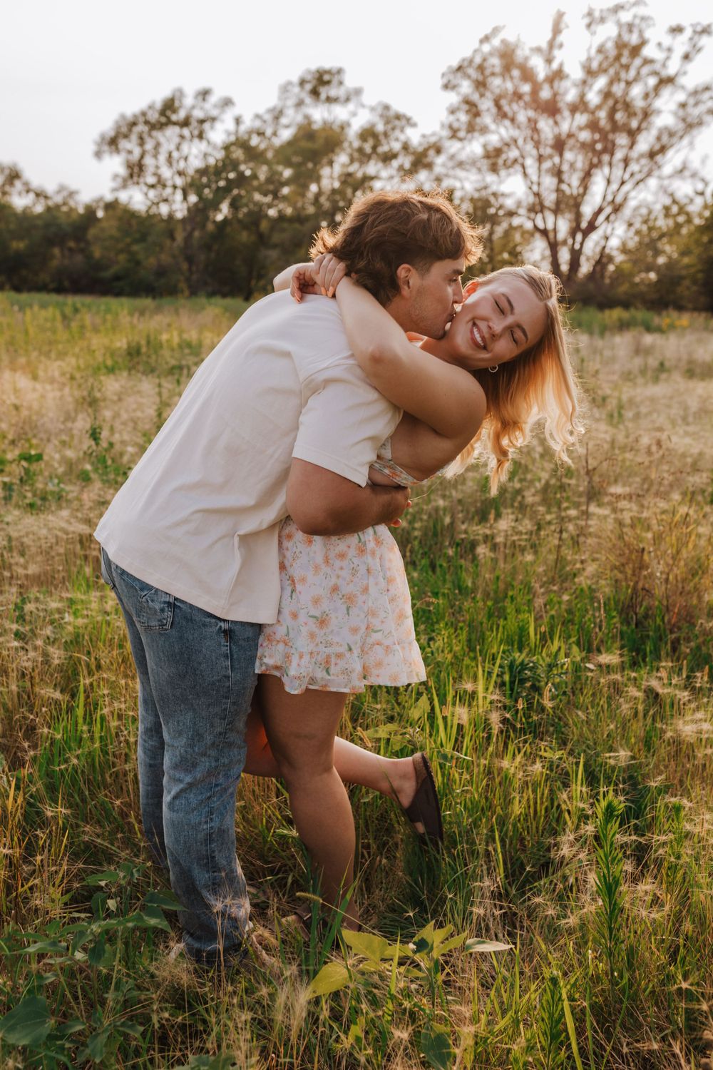 Playful couple embracing in golden field at sunset.