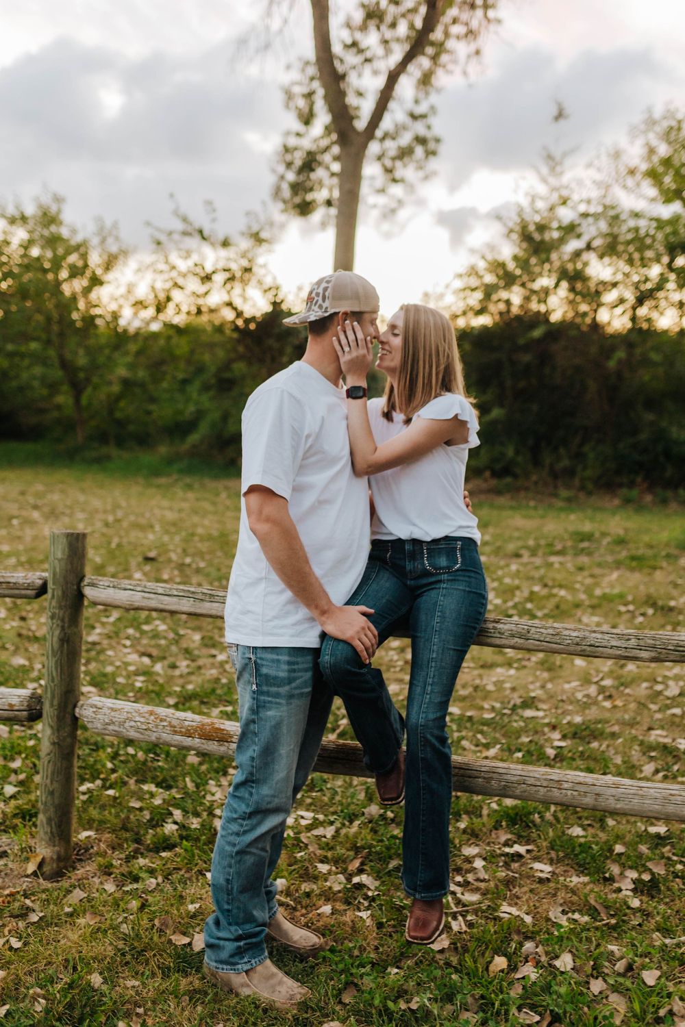 Couple sharing romantic moment on rustic wooden fence at sunset.
