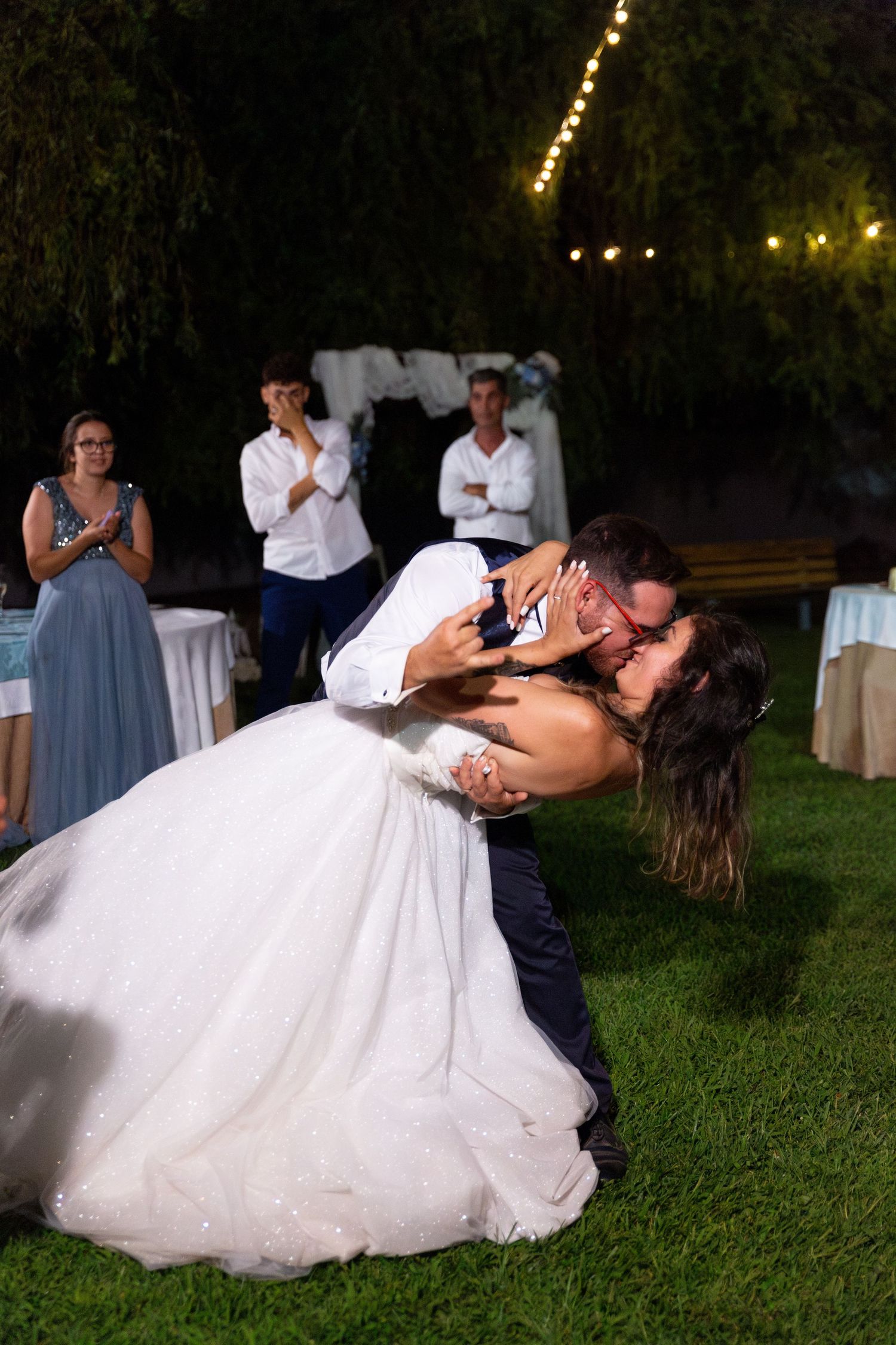 A romantic wedding dance dip under string lights at an outdoor evening reception.