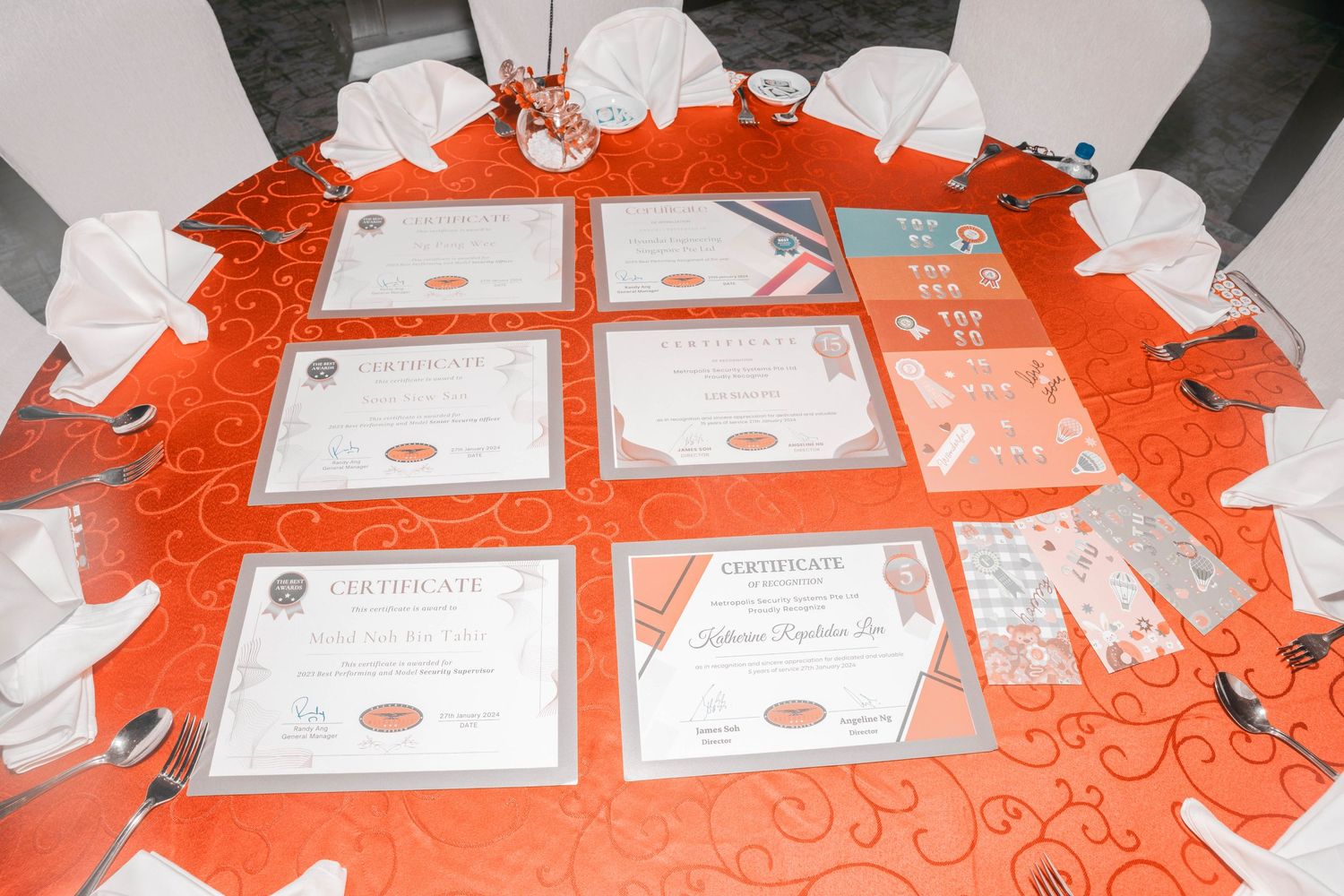 Certificates and awards displayed on an orange tablecloth at a corporate event.