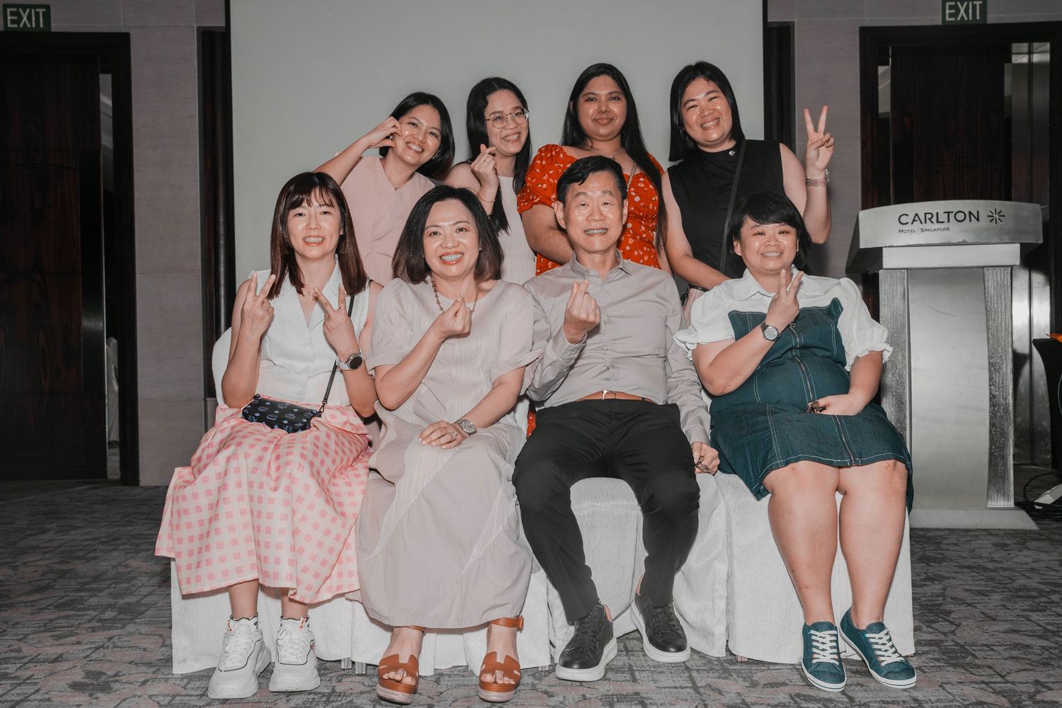 Group posing together on chairs making peace signs during an event.