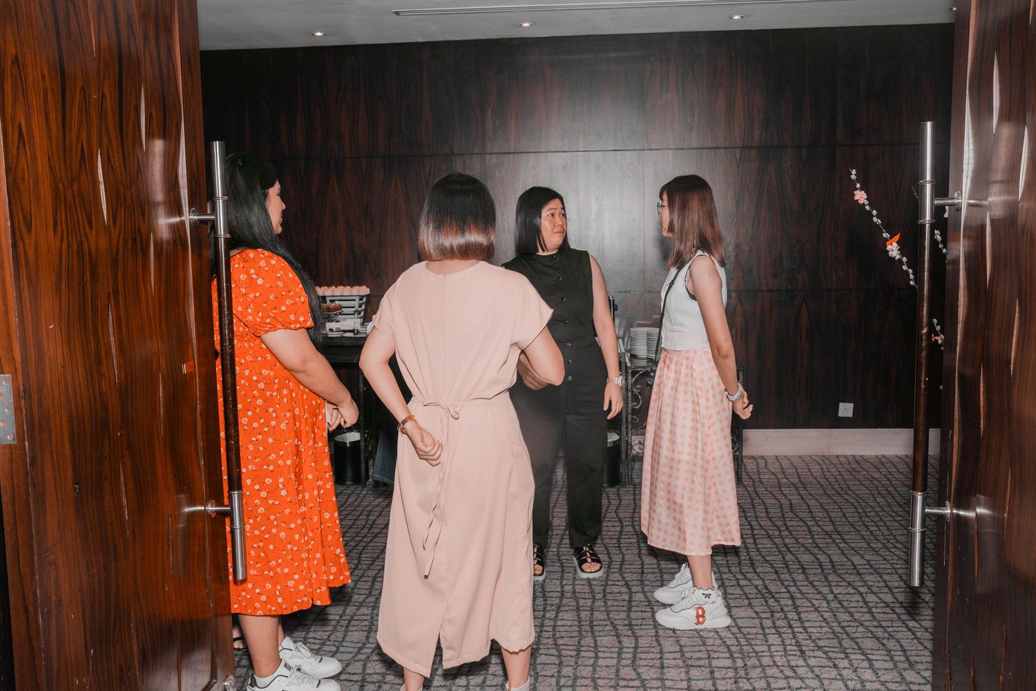 Group of people in casual attire conversing in a wood-paneled hallway.