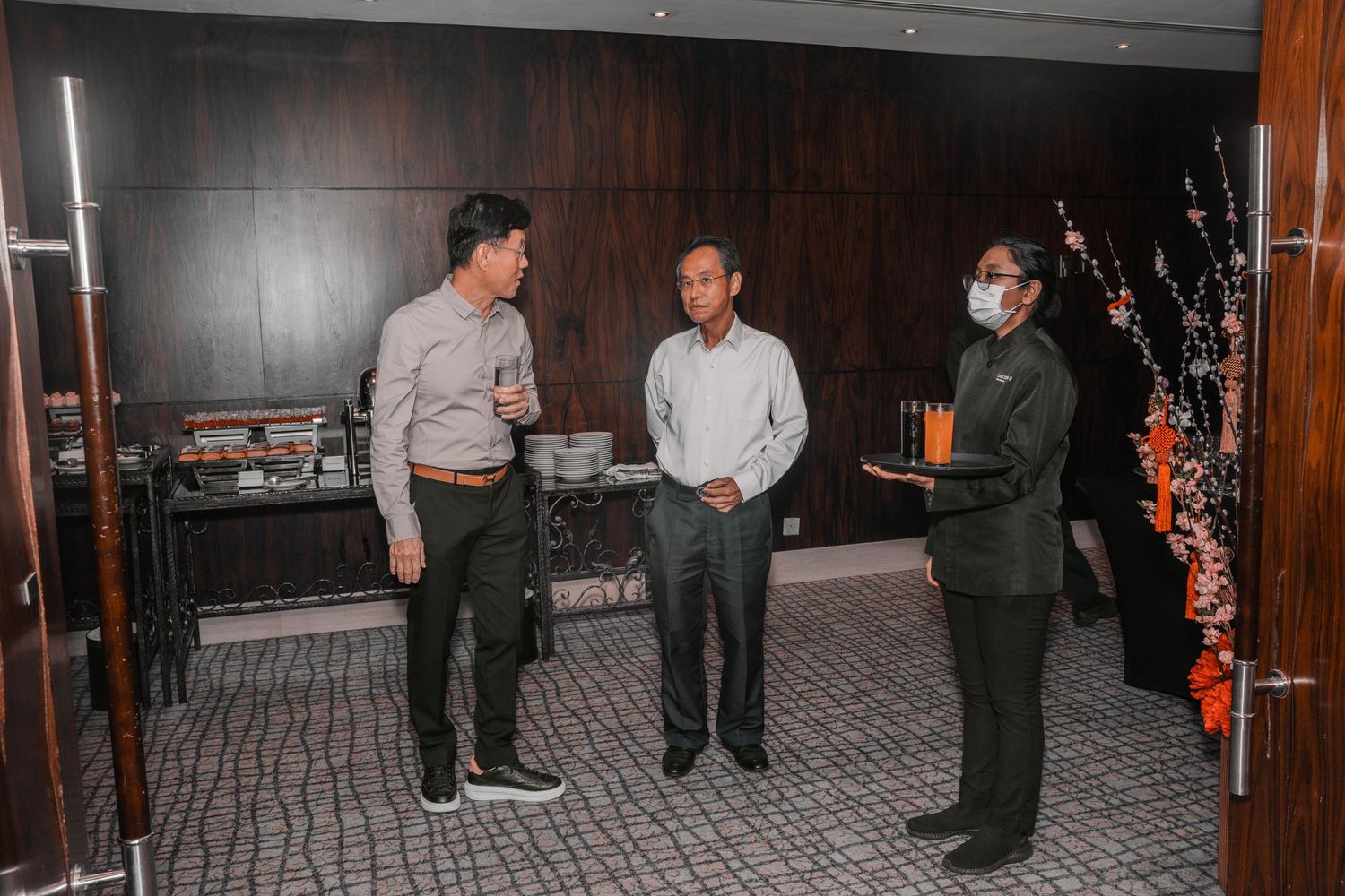 Three people having a conversation in business attire in front of decorative branches.