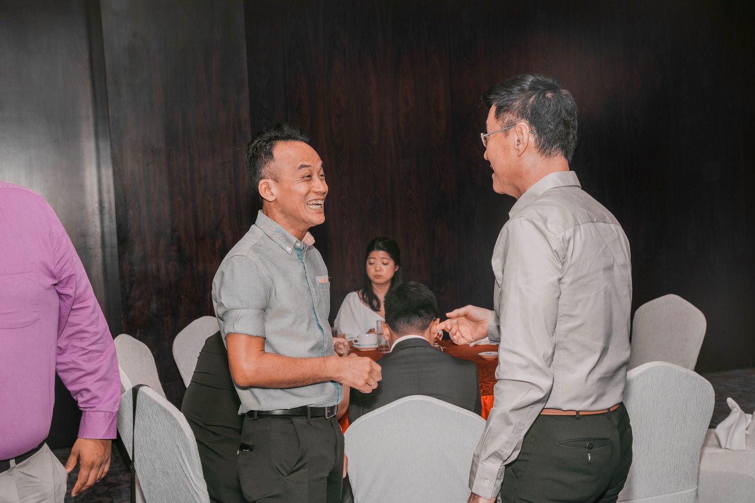 Two people engaged in conversation at formal event with white chairs visible.