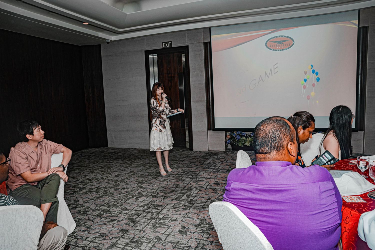 Conference room presentation with attendees seated at tables and a speaker standing.