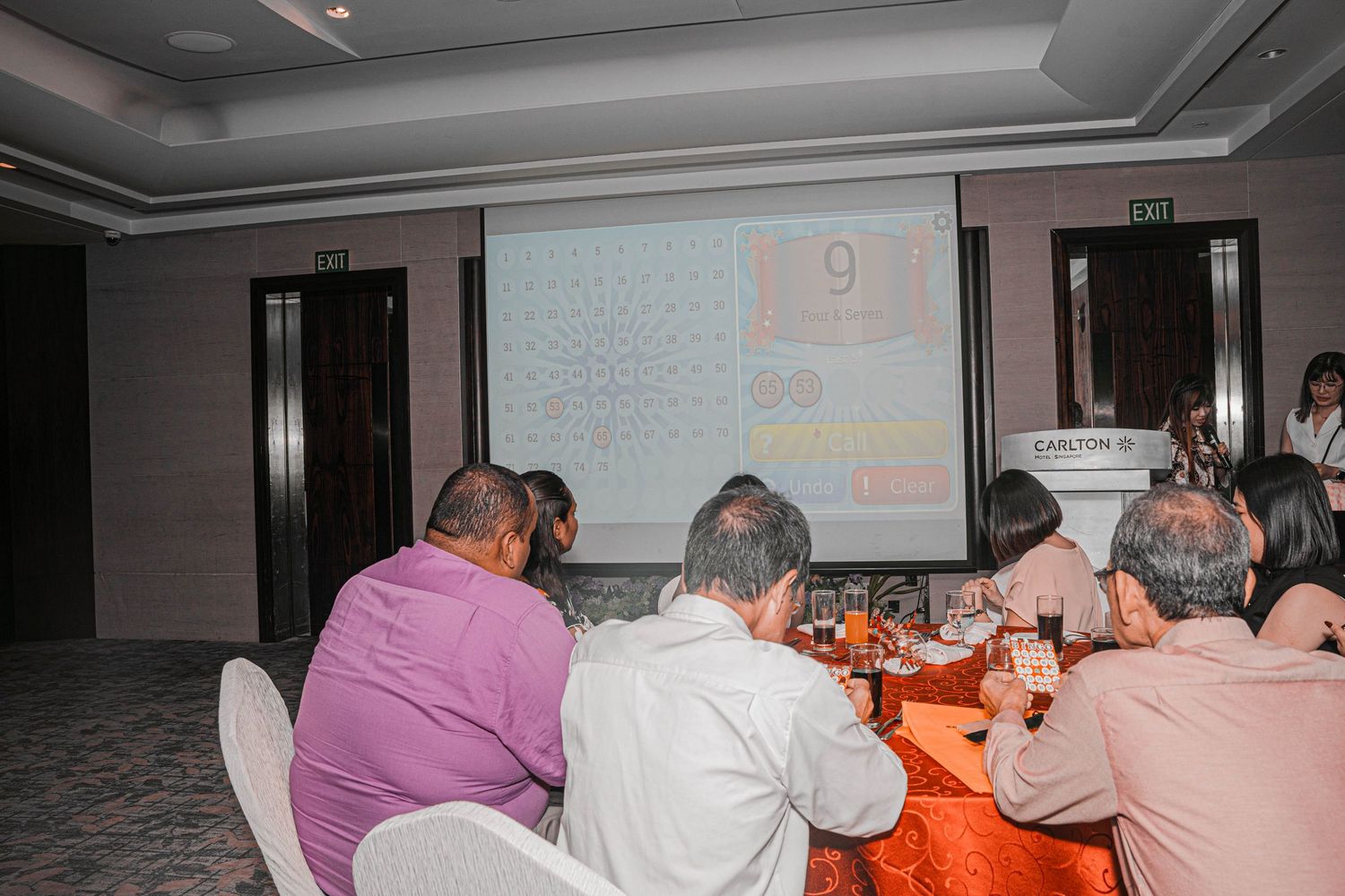 Conference attendees seated at tables with red tablecloths watching a presentation.
