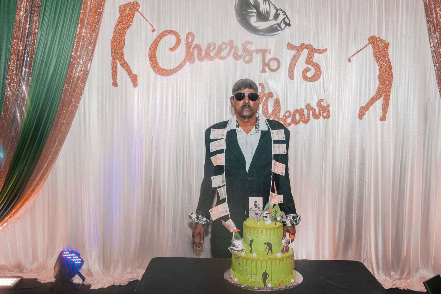 A celebratory event setup with a green cake and golf-themed backdrop reading Cheers to 75 years.