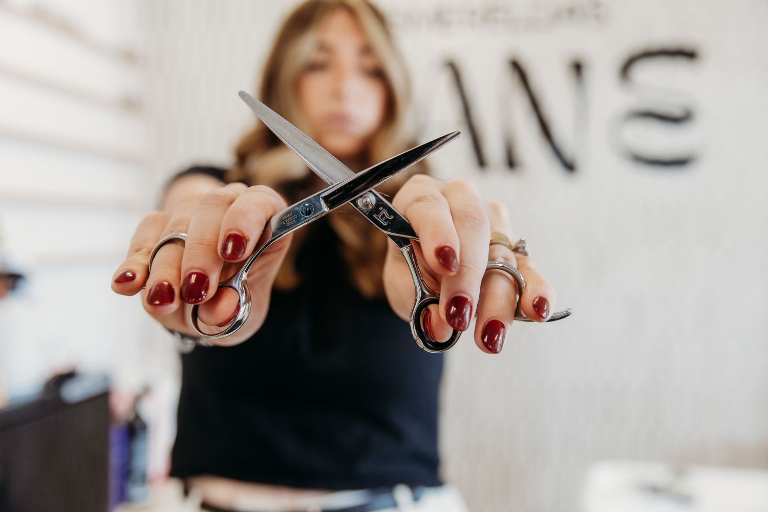Hands with red manicured nails hold up crossed hairdressing scissors against a white background.