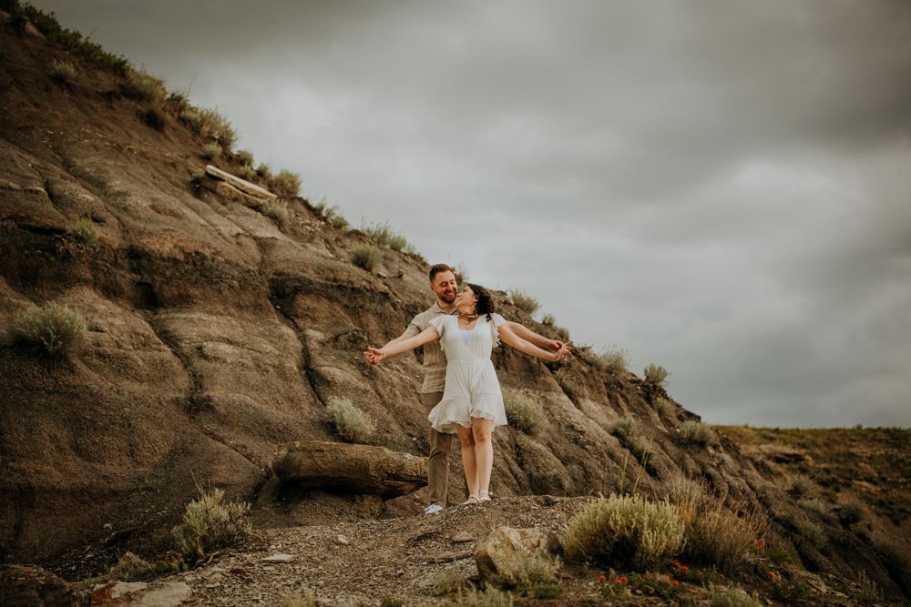 Person in a white dress twirling joyfully on a rugged mountain path at sunset.