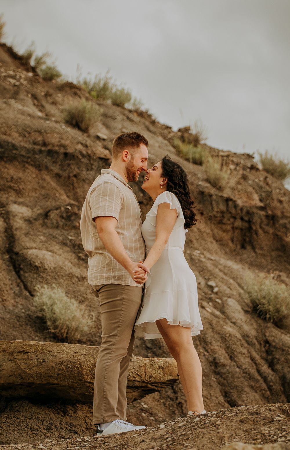 Couple in coordinated white and beige outfits share an intimate moment against rocky desert backdrop.
