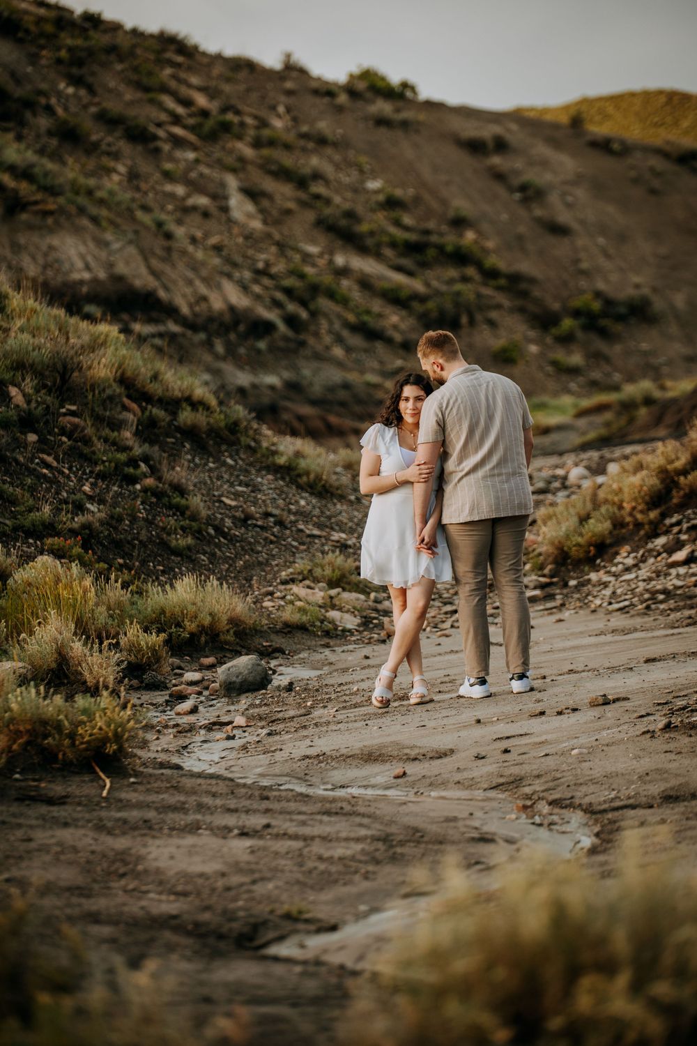 A romantic couple standing on a rocky mountain trail during a moody evening.