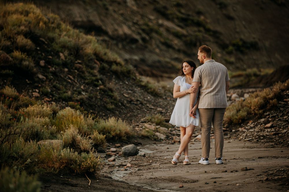 Couple walks hand in hand along a rugged desert path during sunset.
