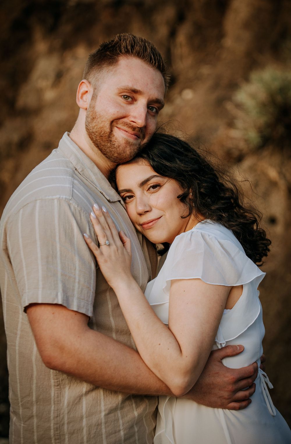 Close-up of couple in white and beige embracing against desert background.