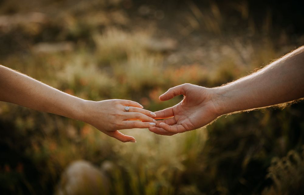 Two hands reaching towards each other against blurred natural backdrop at sunset.