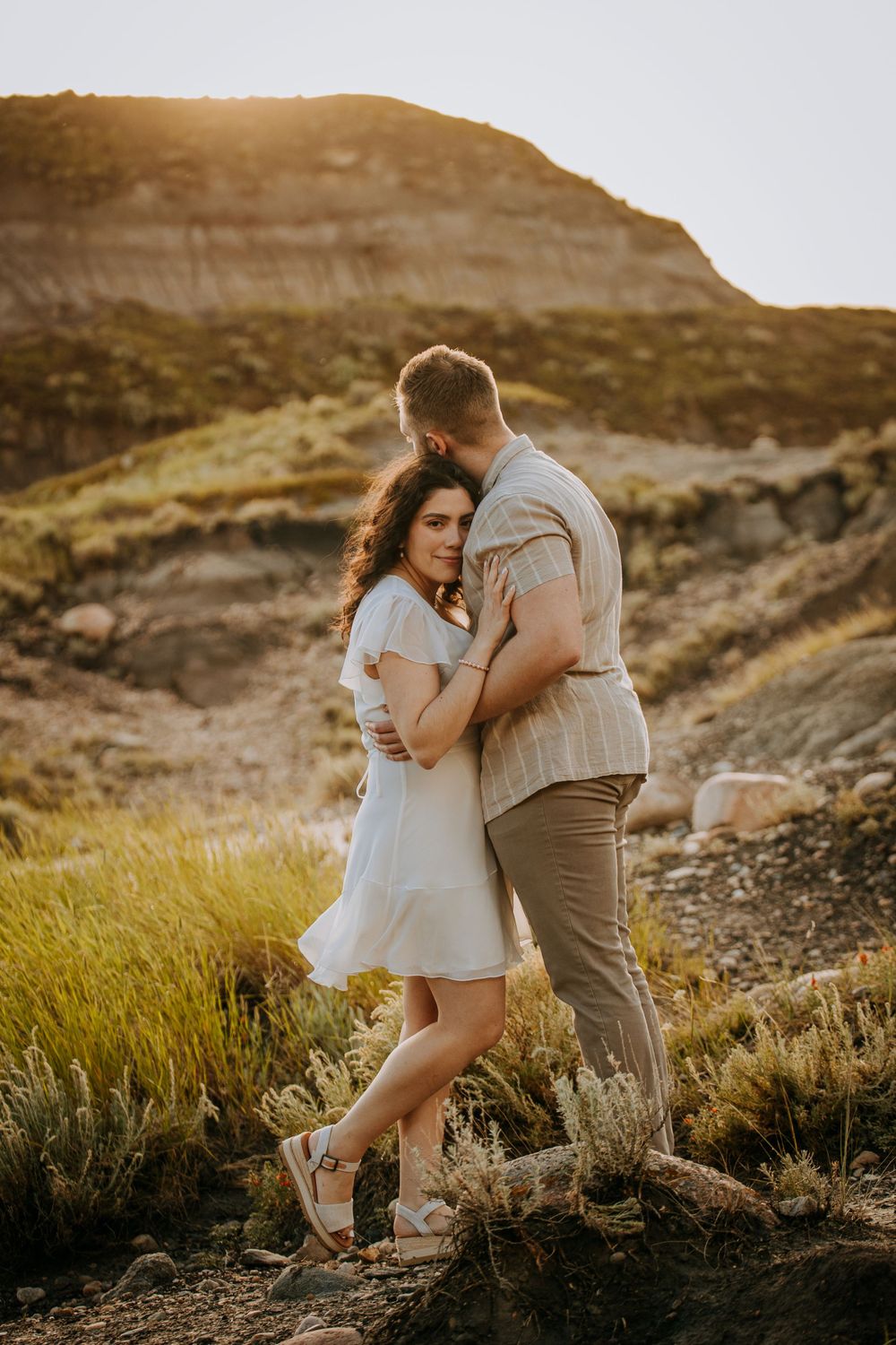 A couple in casual elegant attire embracing against a scenic desert mountain backdrop.