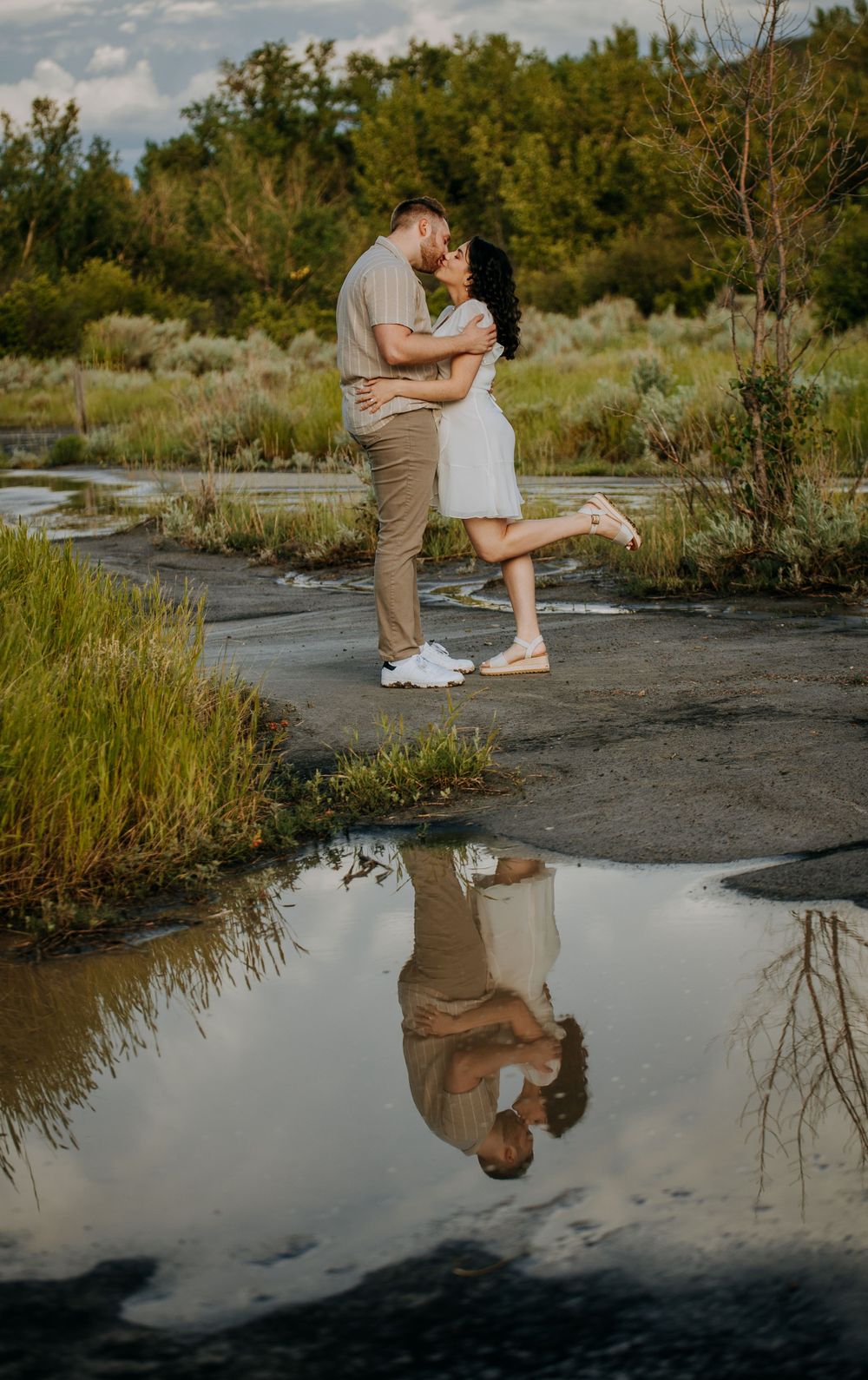Romantic couple embraces on rocky terrain with their reflection captured in a puddle during golden hour.